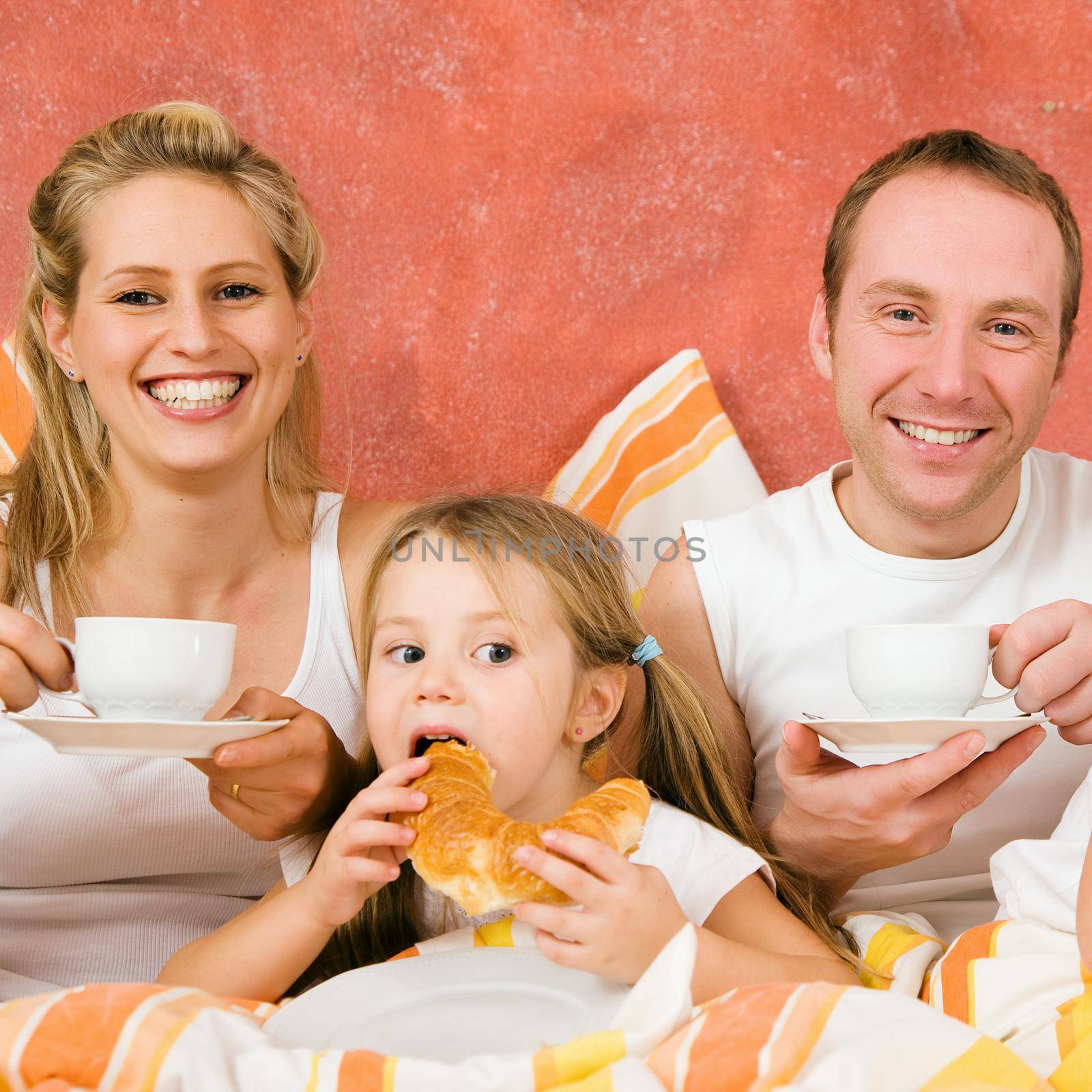 Family of three in bed having breakfast by Kzenon