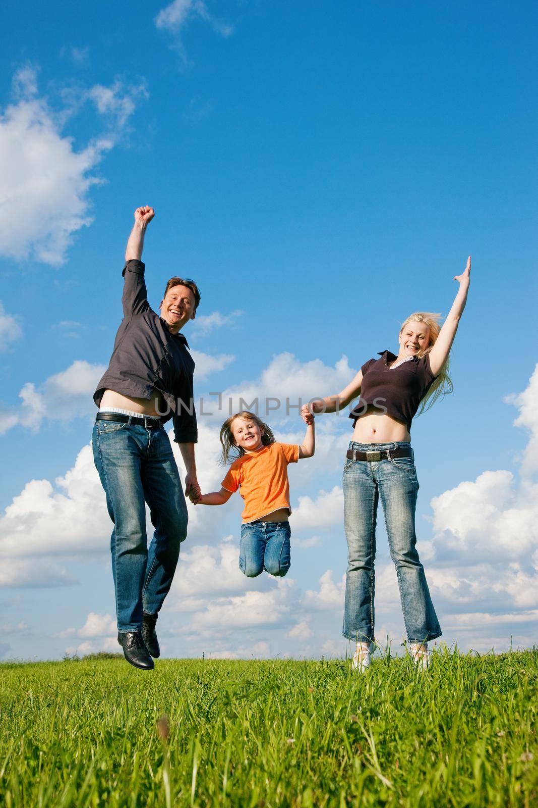 Family - mother, father, child - jumping high in the air on a green meadow at a late summer afternoon
