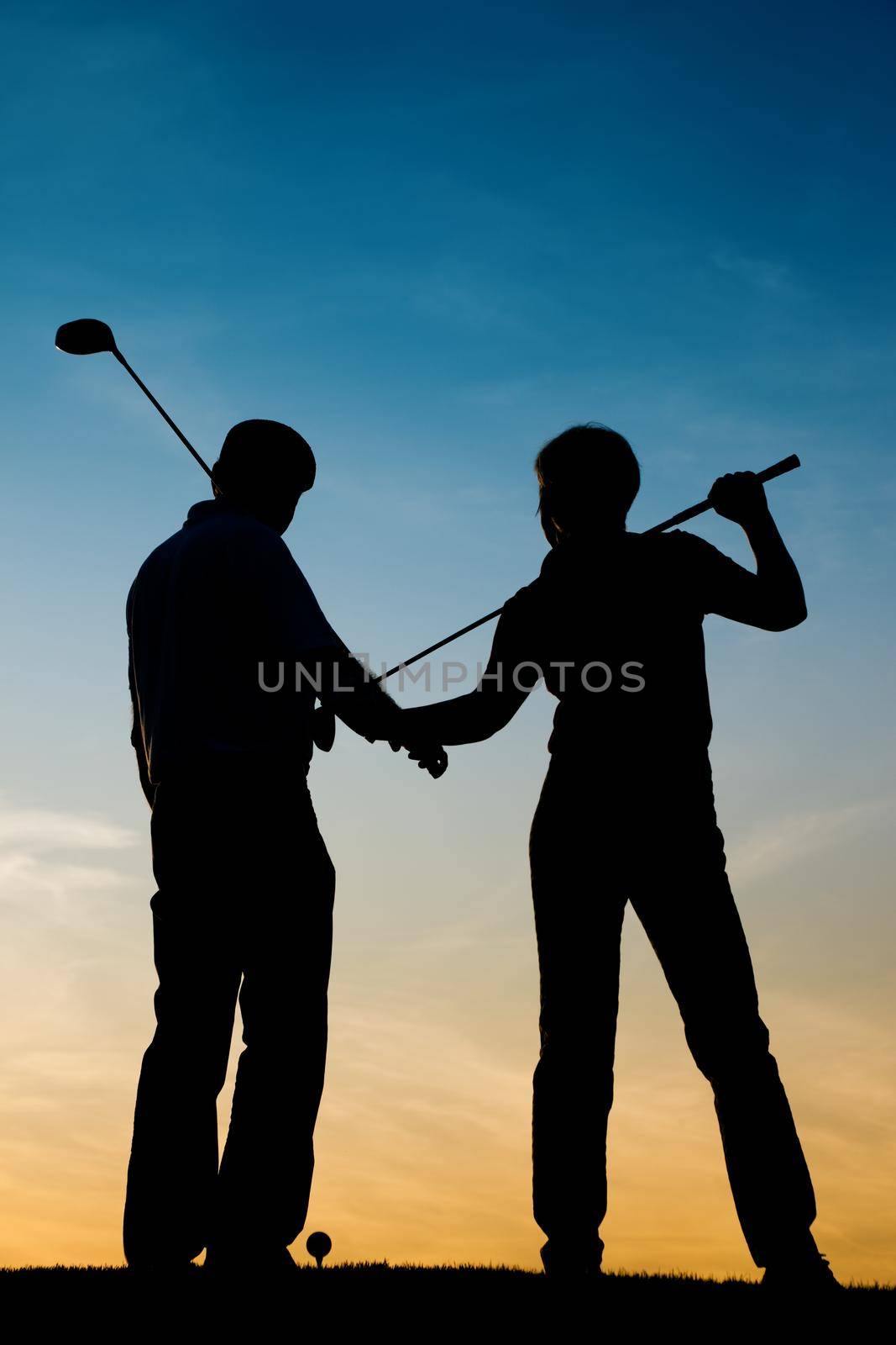 Mature or senior couple playing golf - pictured as a silhouette against an evening sky