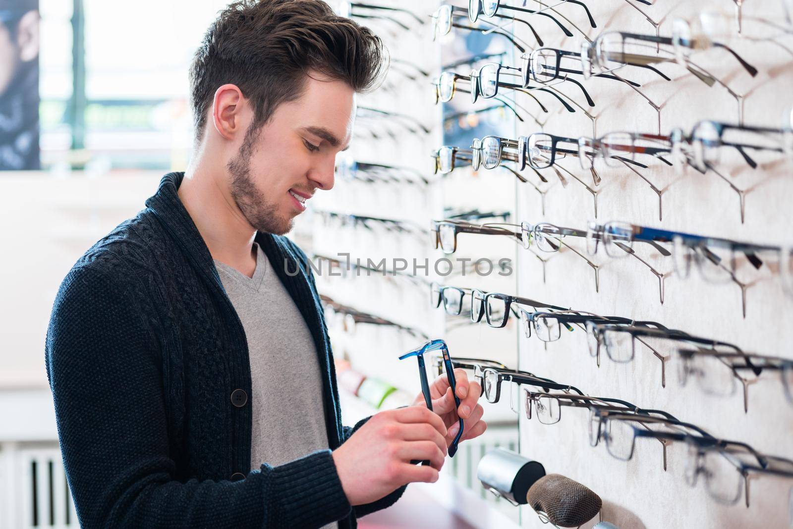 Man choosing glasses from shelf in optician shop by Kzenon