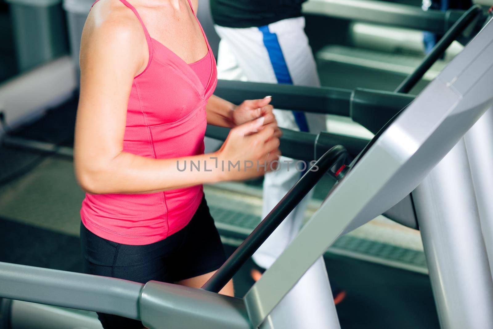 Woman and man in gym - only body to be seen - exercising running on the treadmill to gain more fitness; motion blur in limbs for dynamic