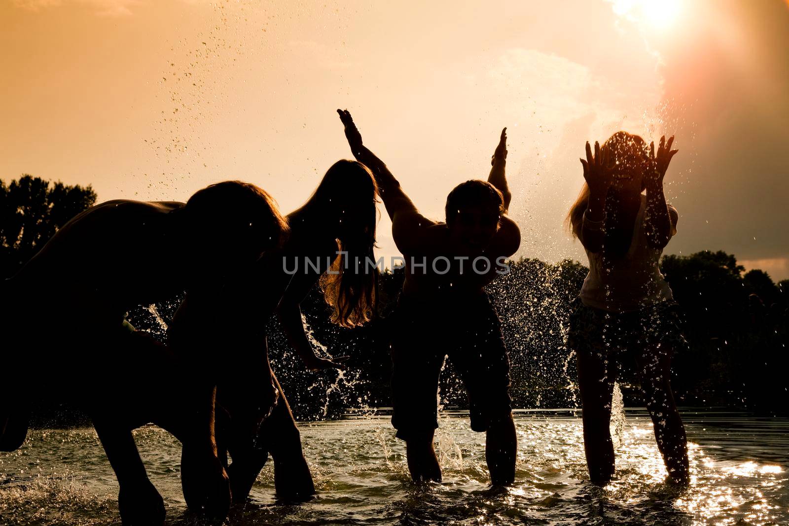 People (two couples) feeling very free in the sunset standing in the water splashing water at each other having an unbelievable amount of fun. Silhouettes