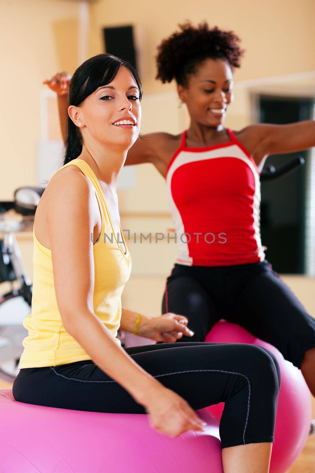 Two young, healthy women doing gymnastics exercises with a fitness ball in gym