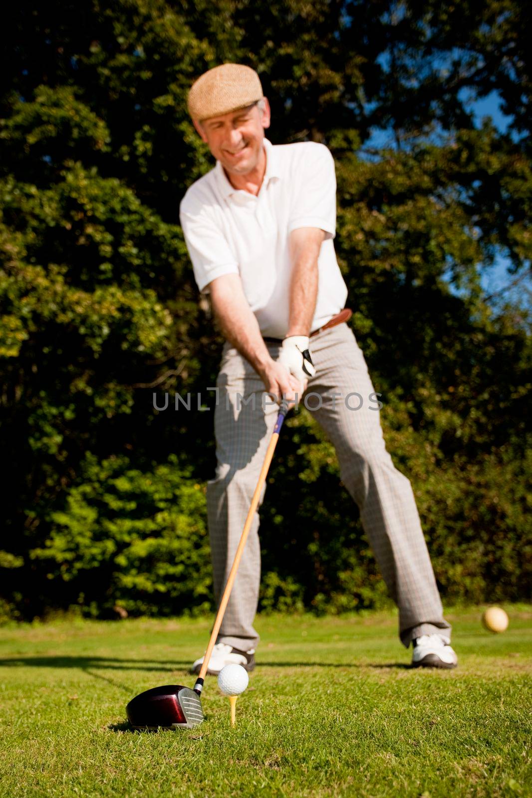 Senior man playing golf attempting the tee stroke in the teeing area (focus is on the ball!)