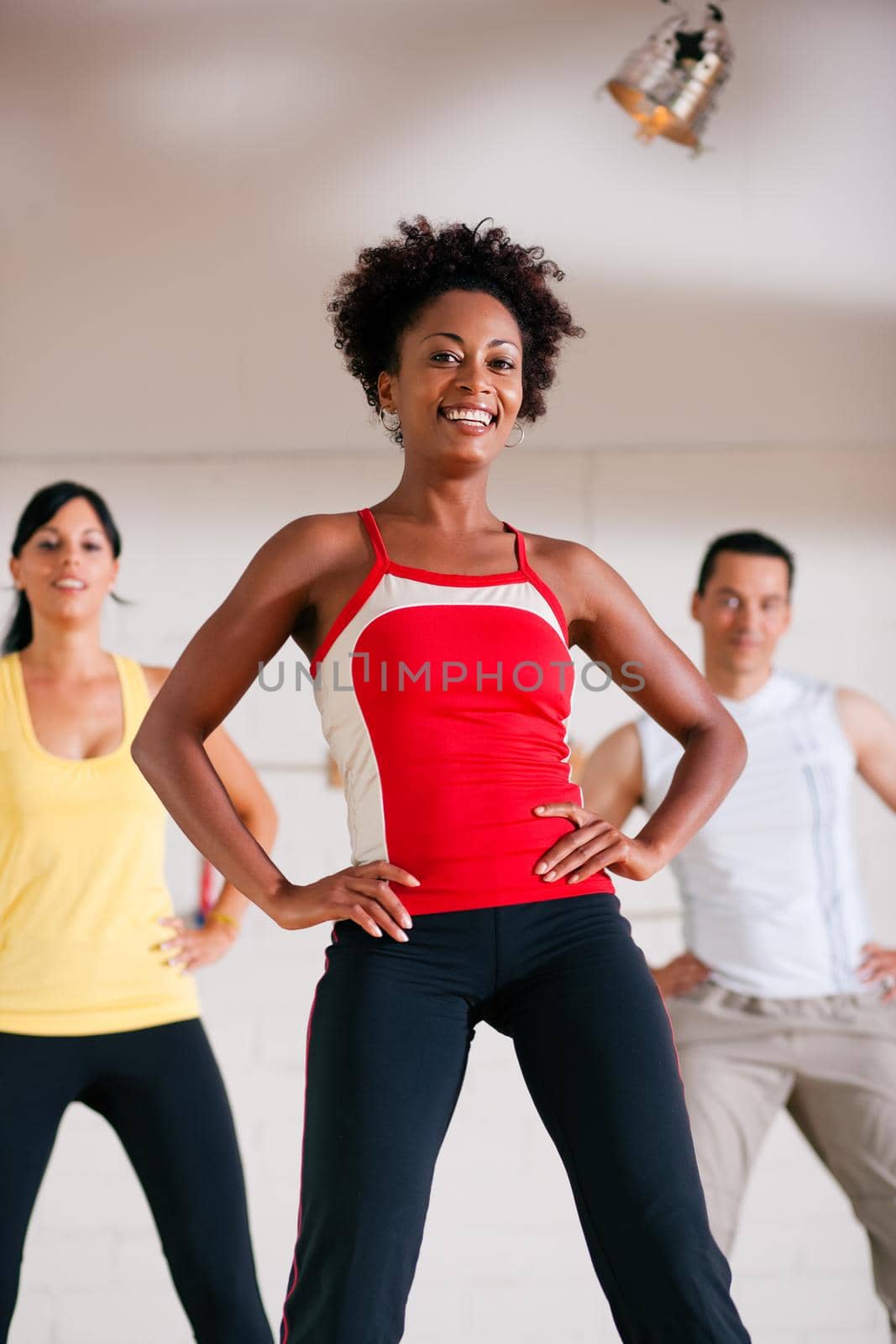 Group of three people in colorful cloths in a gym doing step gymnastics, a female instructor in front