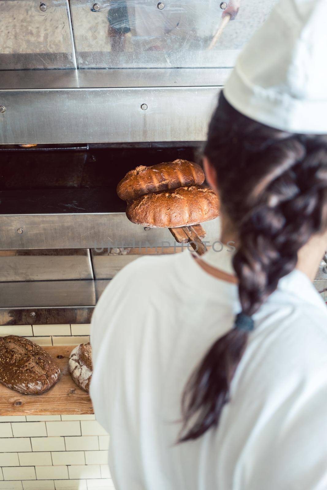 Baker woman getting fresh bread with shovel out of oven