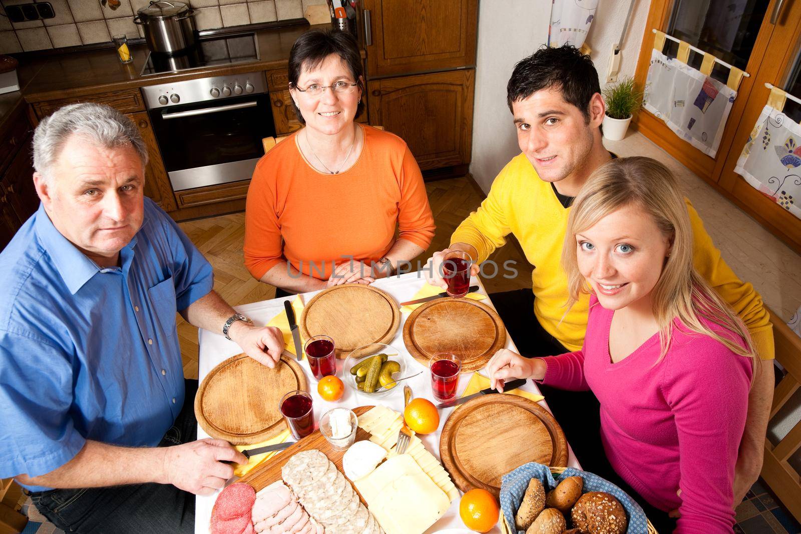 Family with adult kids having a meal with bread, cold cuts, and cheese