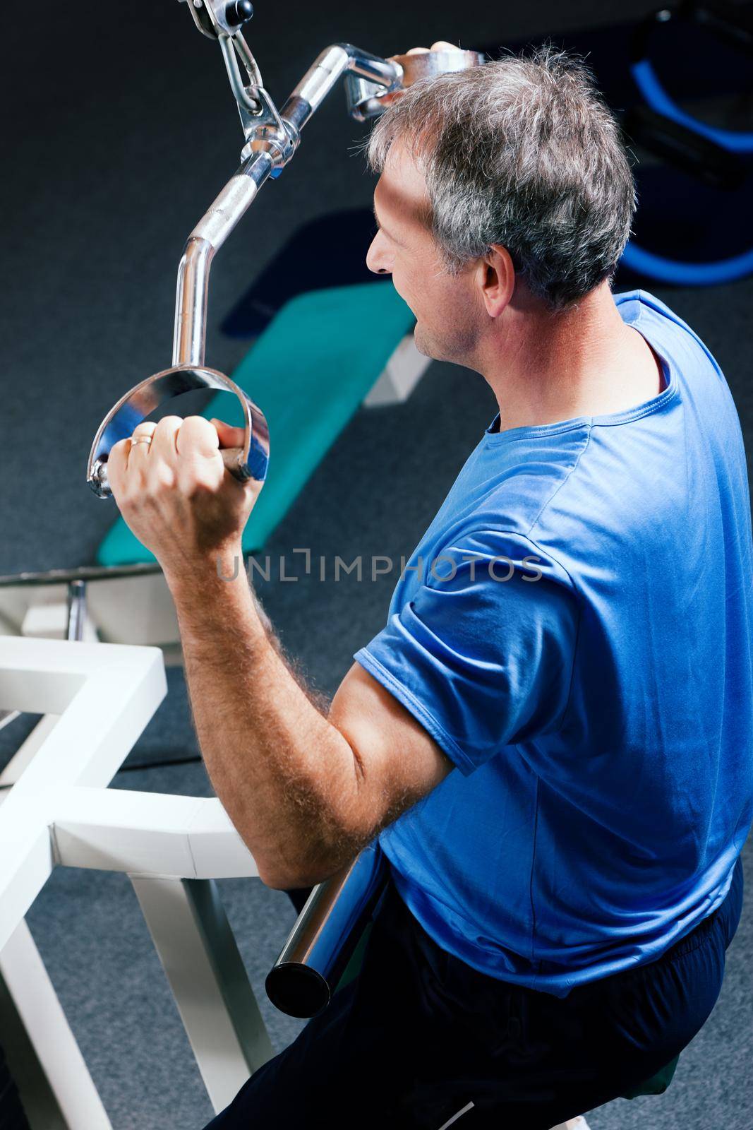 Senior man in the gym lifting weights on a lat pull machine, exercising