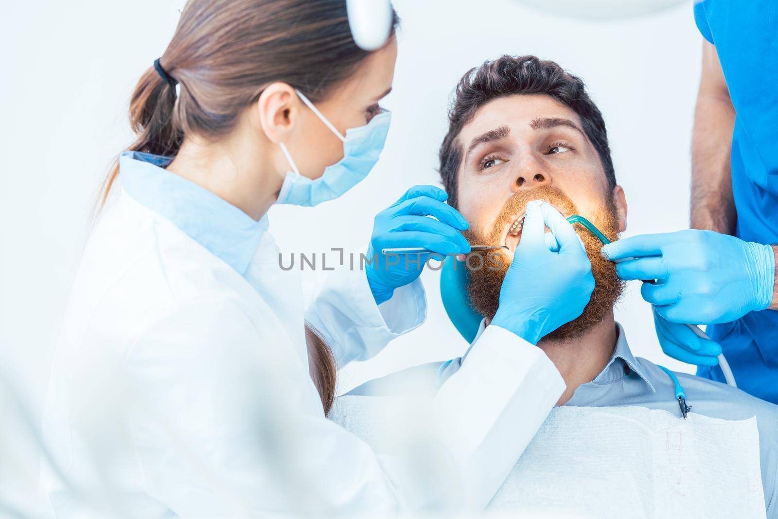 Portrait of a young man looking at camera with a relaxed facial expression, during a painless oral procedure in the modern dental office of an experienced dentist