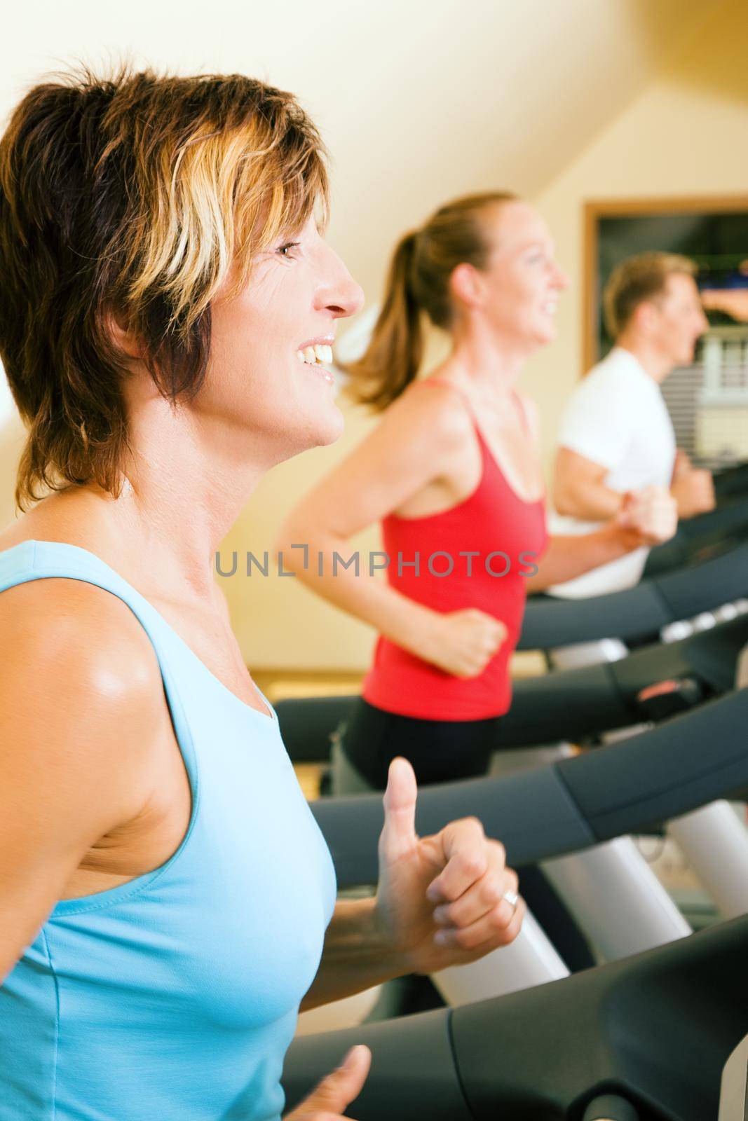 Three happy people running on a treadmill in a gym; slight motion blur on arms of woman in foreground for a dynamic picture