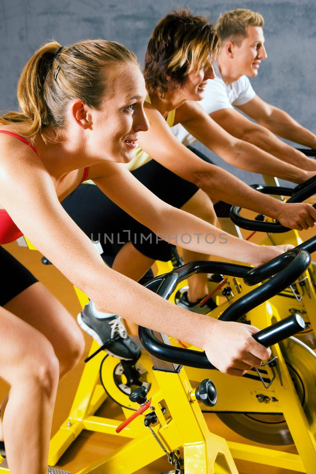 Three people spinning on bicycles in a gym or fitness club for a workout