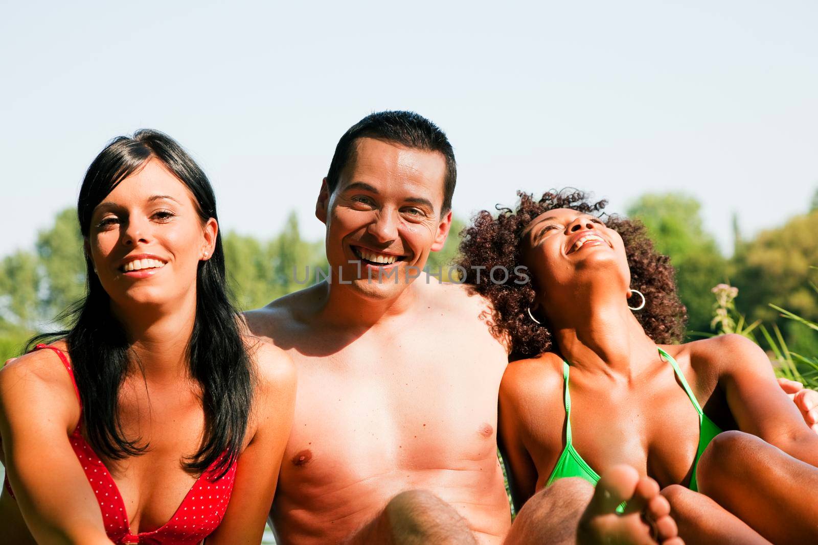 Group of friends - man and to women sitting in the sun in summer and having fun enjoying themselves
