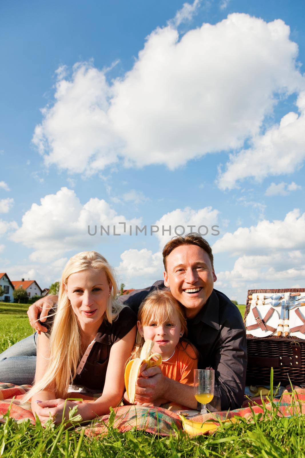 Family - father, mother and daughter child - having a picnic on a green meadow on a beautiful and bright summer day