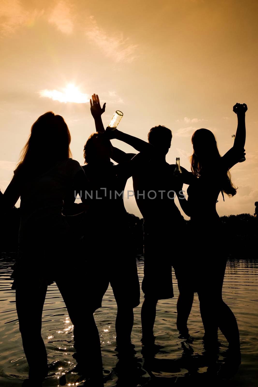 People (two couples) on the beach dancing to music, drinking and having a lot of fun in the sunset - only silhouette of people to be seen