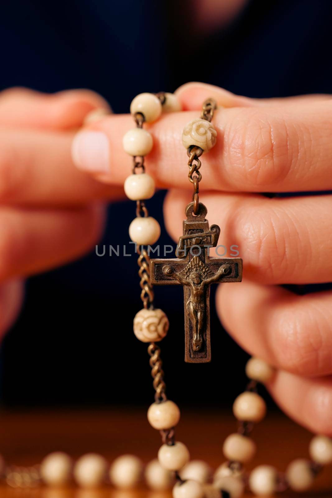 Woman (only closeup of hands to be seen) with rosary sending a prayer to God, the dark setting suggests she is sad or lonely