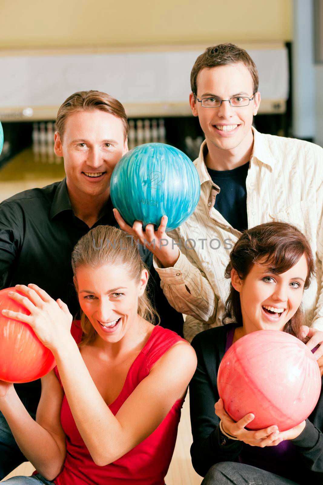 Group of four friends in a bowling alley having fun, holding their bowling balls (focus on girls in front row)