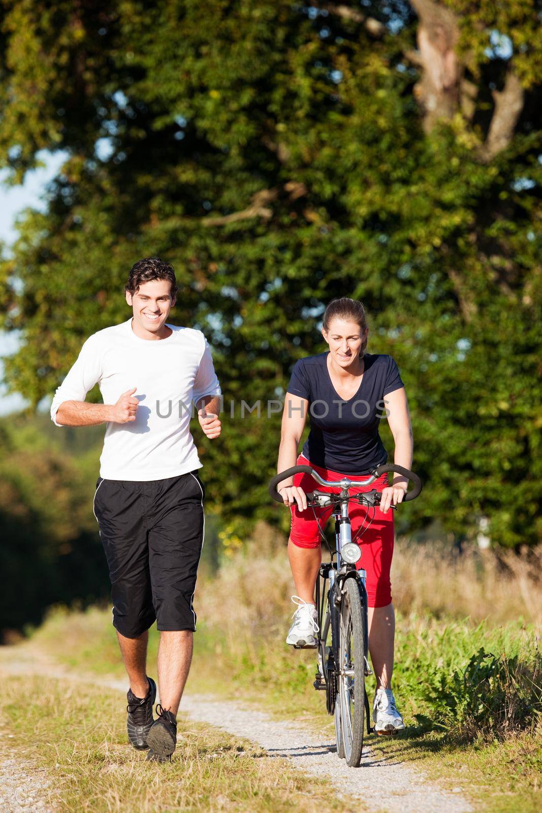 Young fitness couple doing sport outdoors, jogging and riding a bicycle in autumn under a clear blue sky