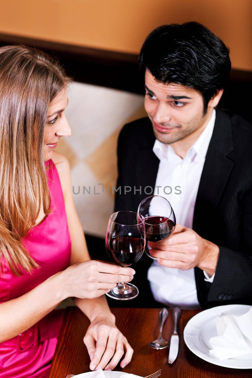 Young couple - man and woman - in a restaurant clinking the red wine glasses; focus on the glasses