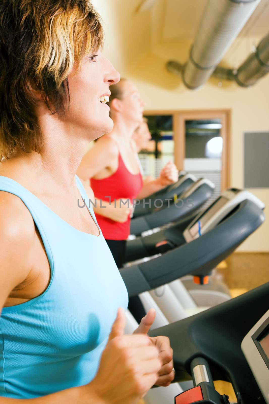 Three happy people running on a treadmill in a gym; slight motion blur on arms of woman in foreground for a dynamic picture