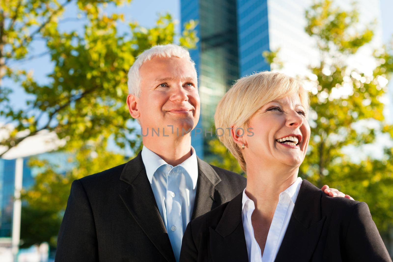 Business people - mature or senior - standing in a park outdoors in front of a office building