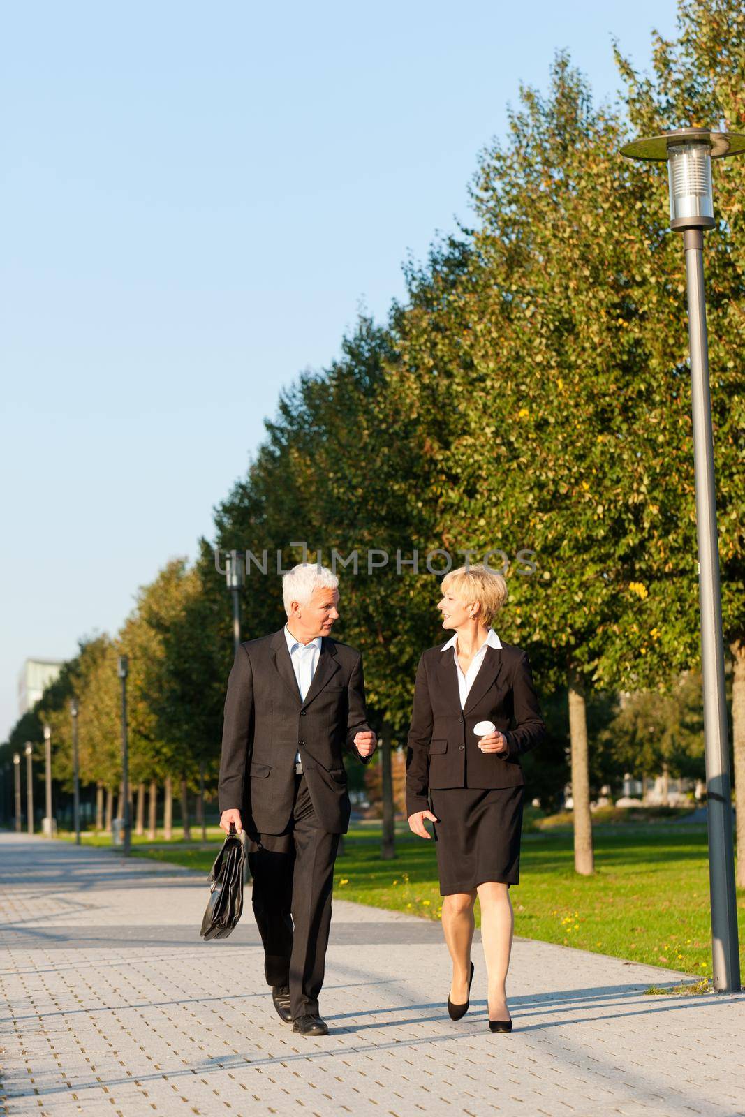 Business people - mature or senior - talking outdoors and walking in a park