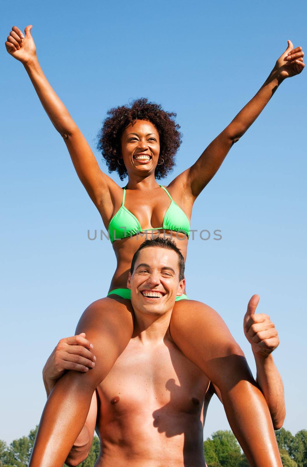 Couple in love - Woman of color in bikini sitting on her man’s shoulders under blue sky - summer and fun