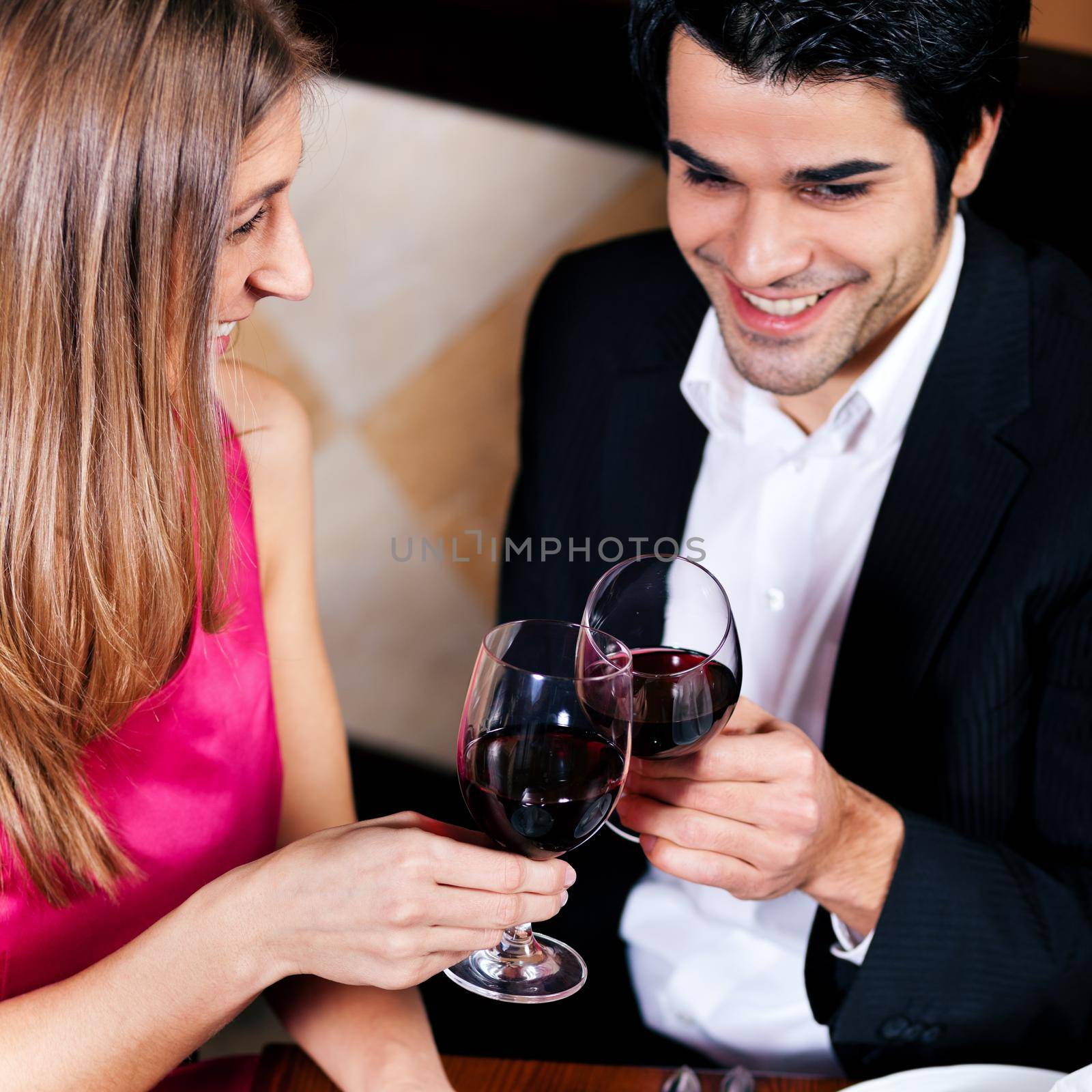 Young couple - man and woman - in a restaurant clinking the red wine glasses; focus on the glasses