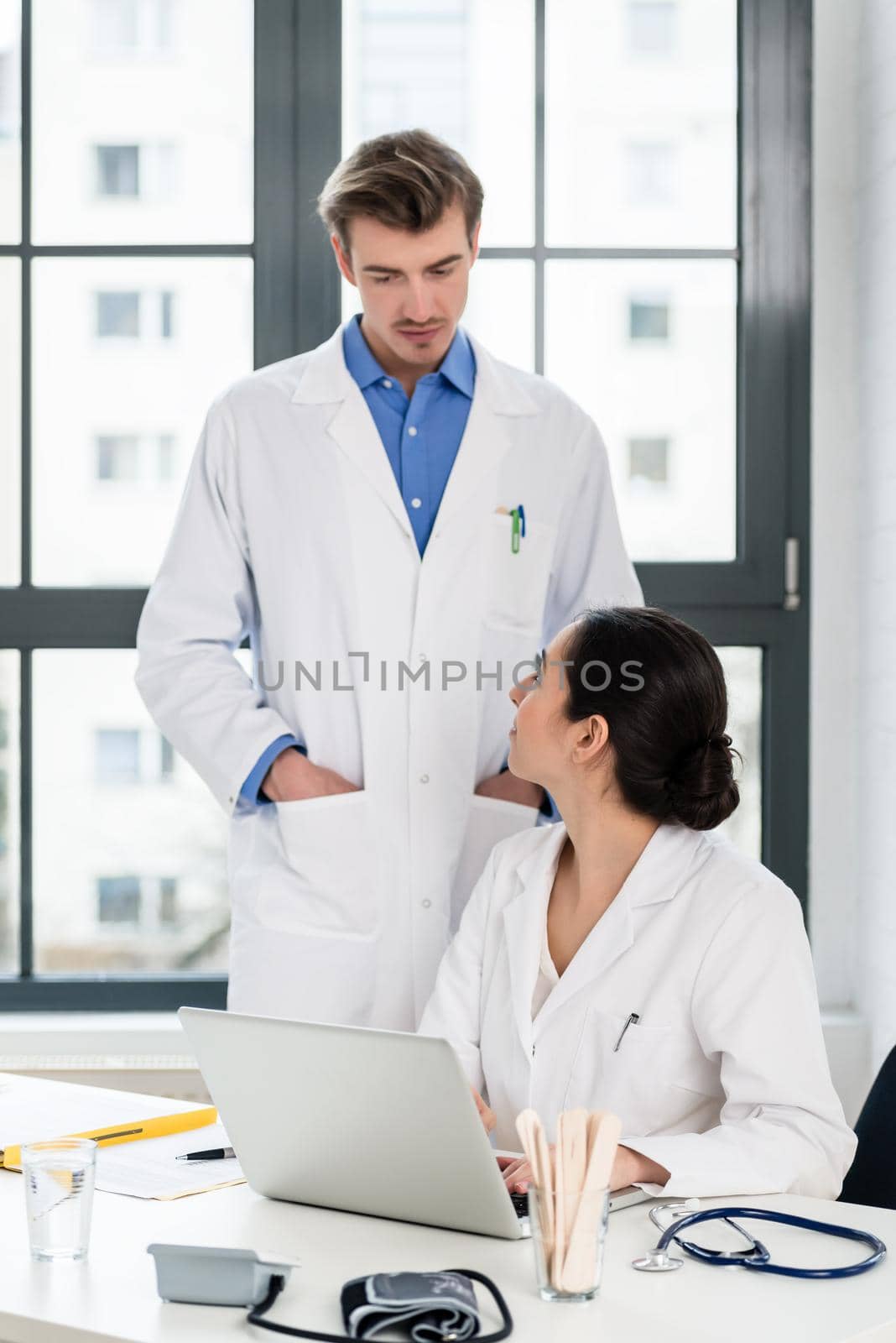 Experienced doctor and pharmacist checking together electronic information on a laptop in the office of a hospital with modern equipment