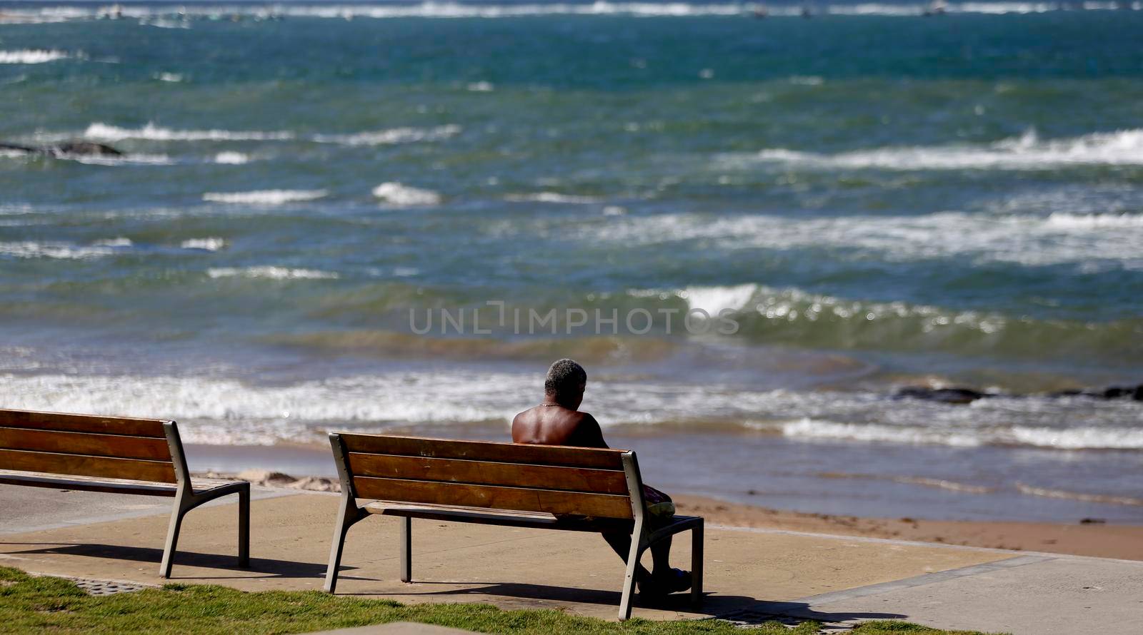 salvador, bahia / brazil - june 6, 2018: Man is seen sitting on a bench facing Itapua beach in the city of Salvador.