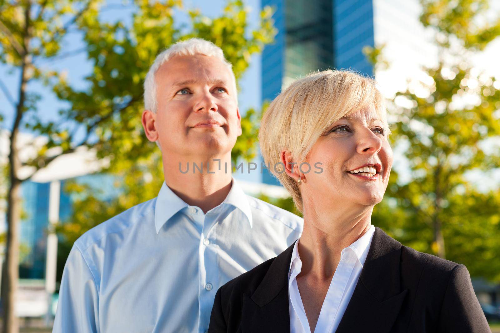 Business people - mature or senior - standing in a park outdoors in front of a office building