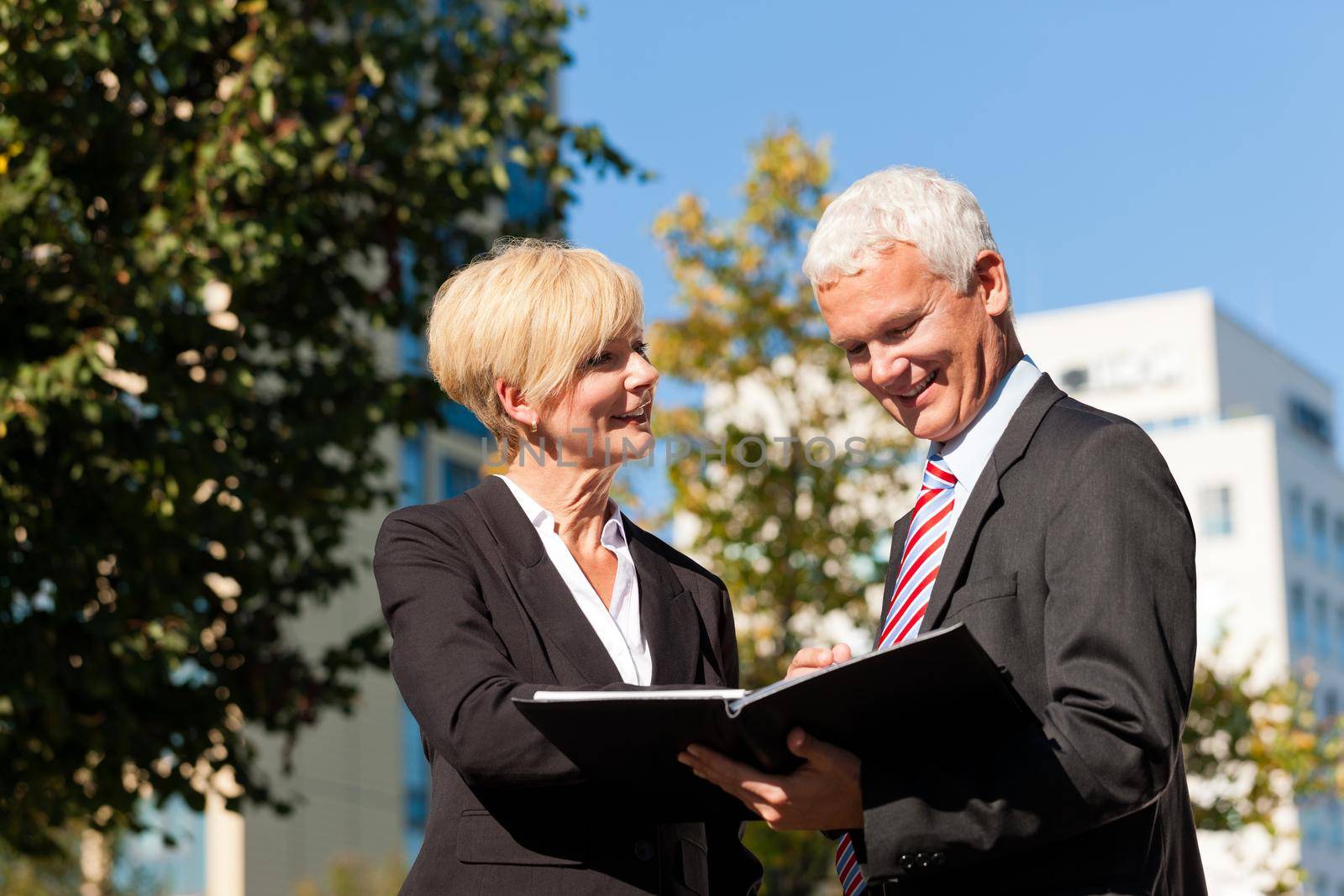 Business people - mature or senior - talking outdoors and discussing a document