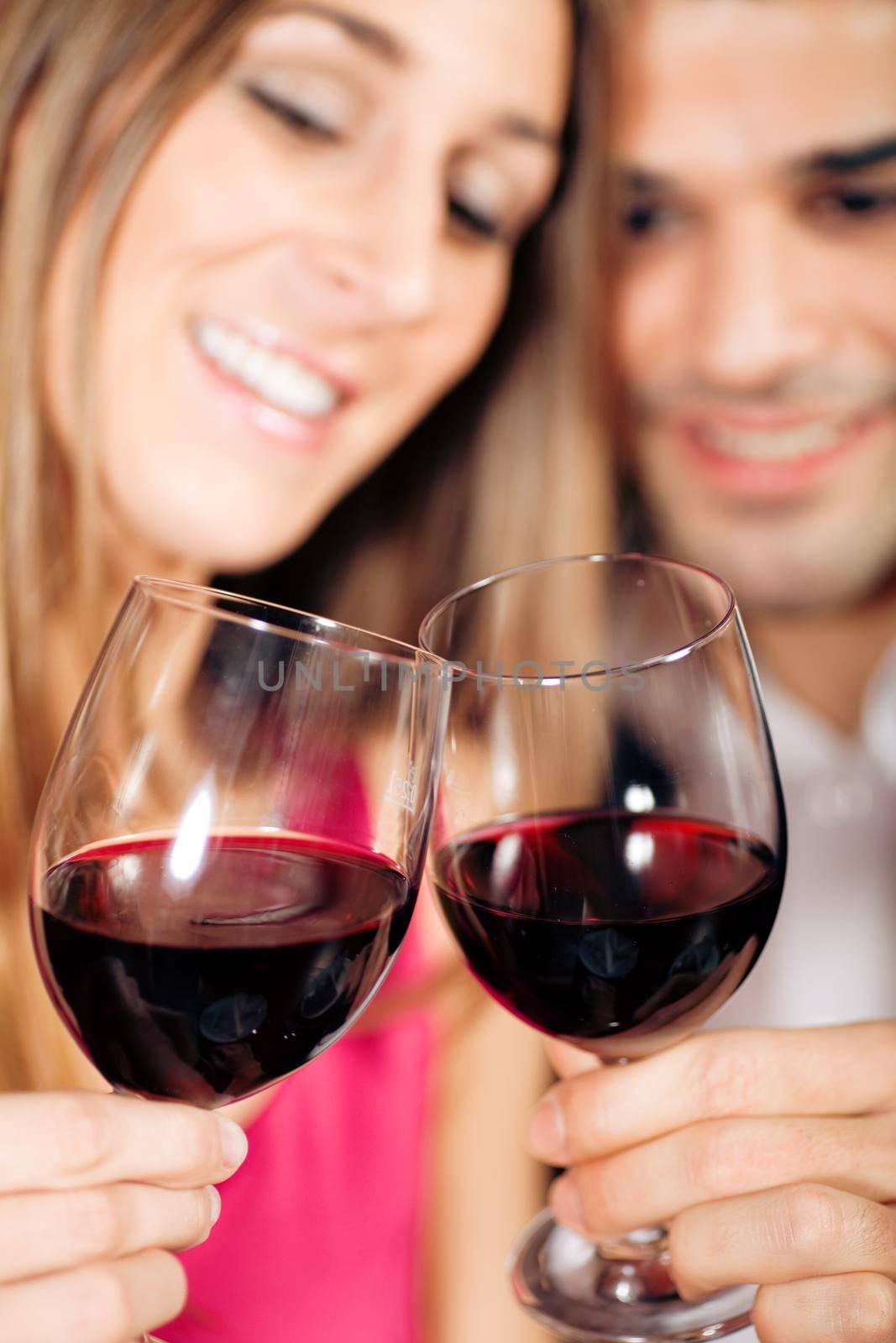 Young couple - man and woman - in a restaurant clinking the red wine glasses; focus on the glasses