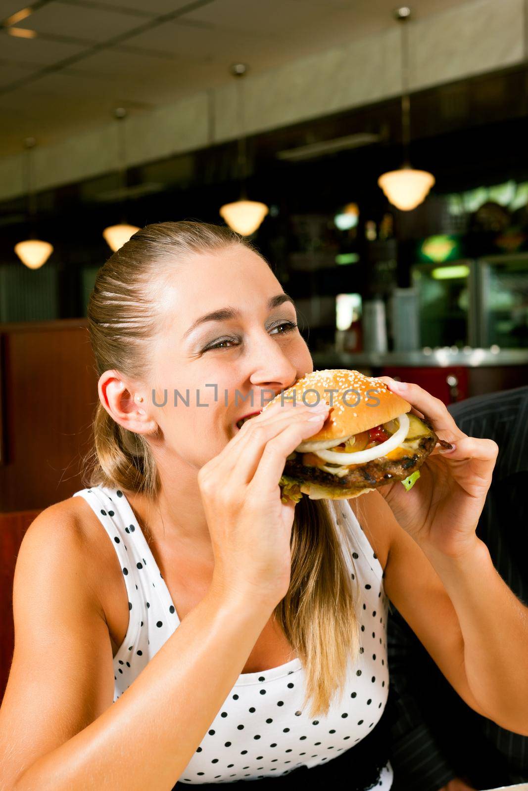 Happy woman in a fast food restaurant eating a hamburger and seems to enjoy it