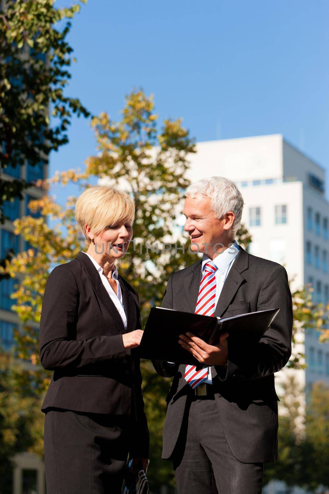 Business people - mature or senior - talking outdoors and discussing a document