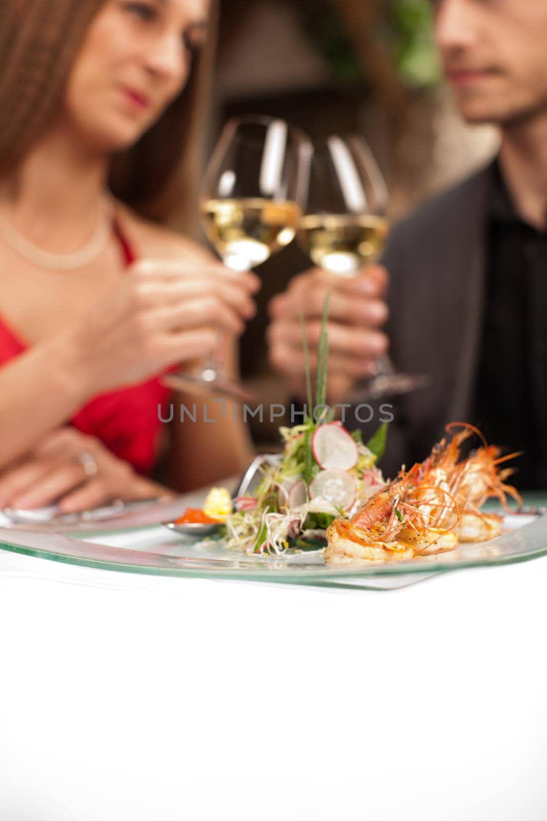 Focus on fresh prawns on plate with couple toasting in background.