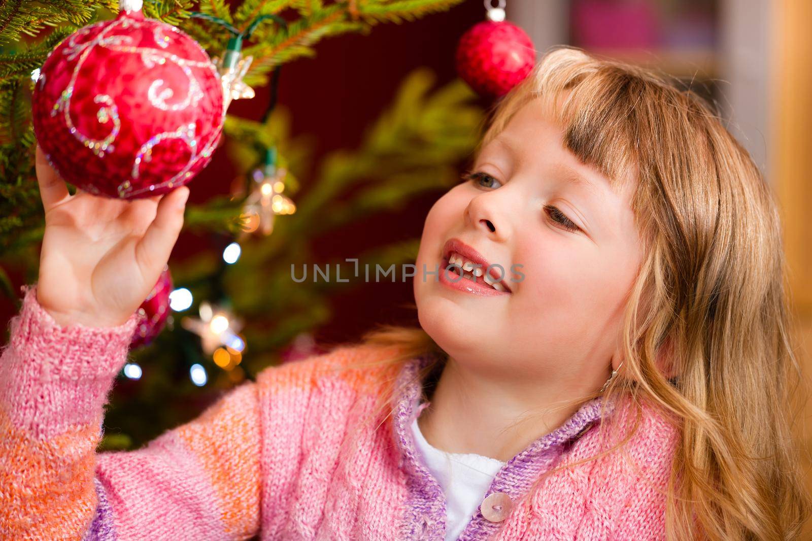 Young girl helping decorating the Christmas tree, holding some Christmas baubles in her hand