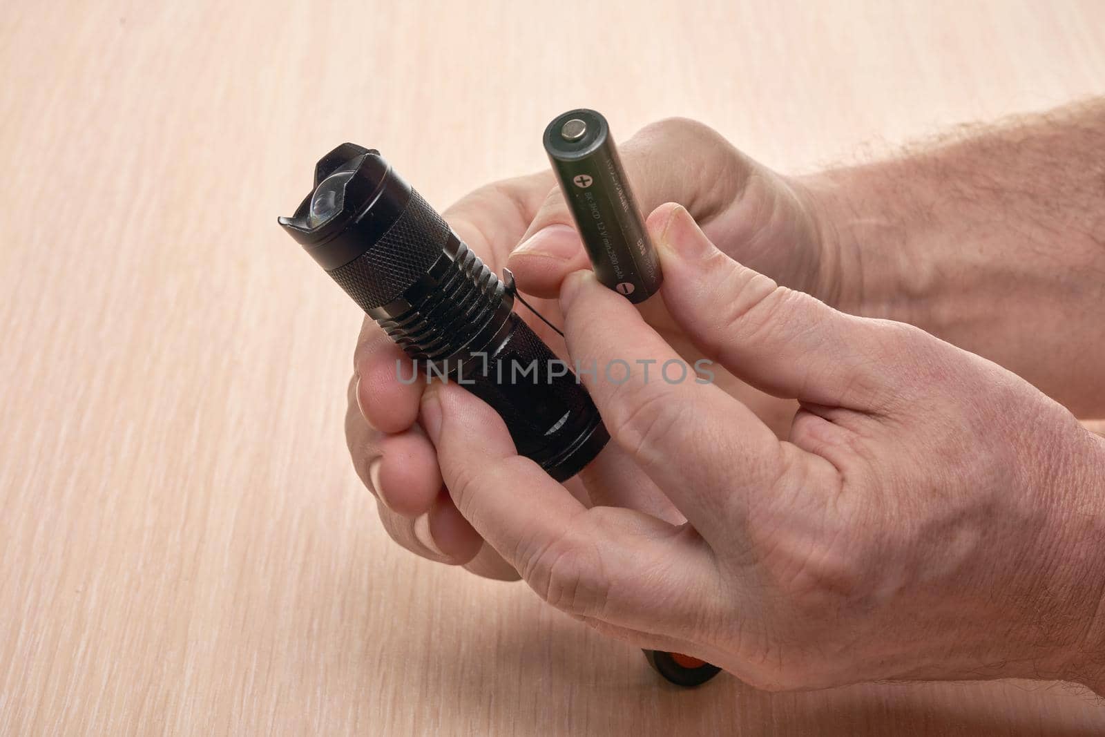 Hands hold a small black flashlight and replace the battery in it by vizland