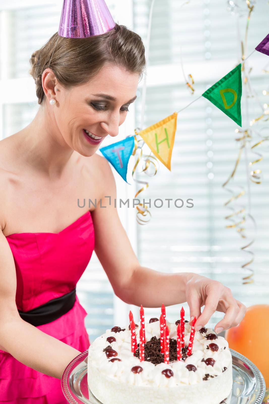 Portrait of a beautiful woman smiling while putting red candles on cake by Kzenon