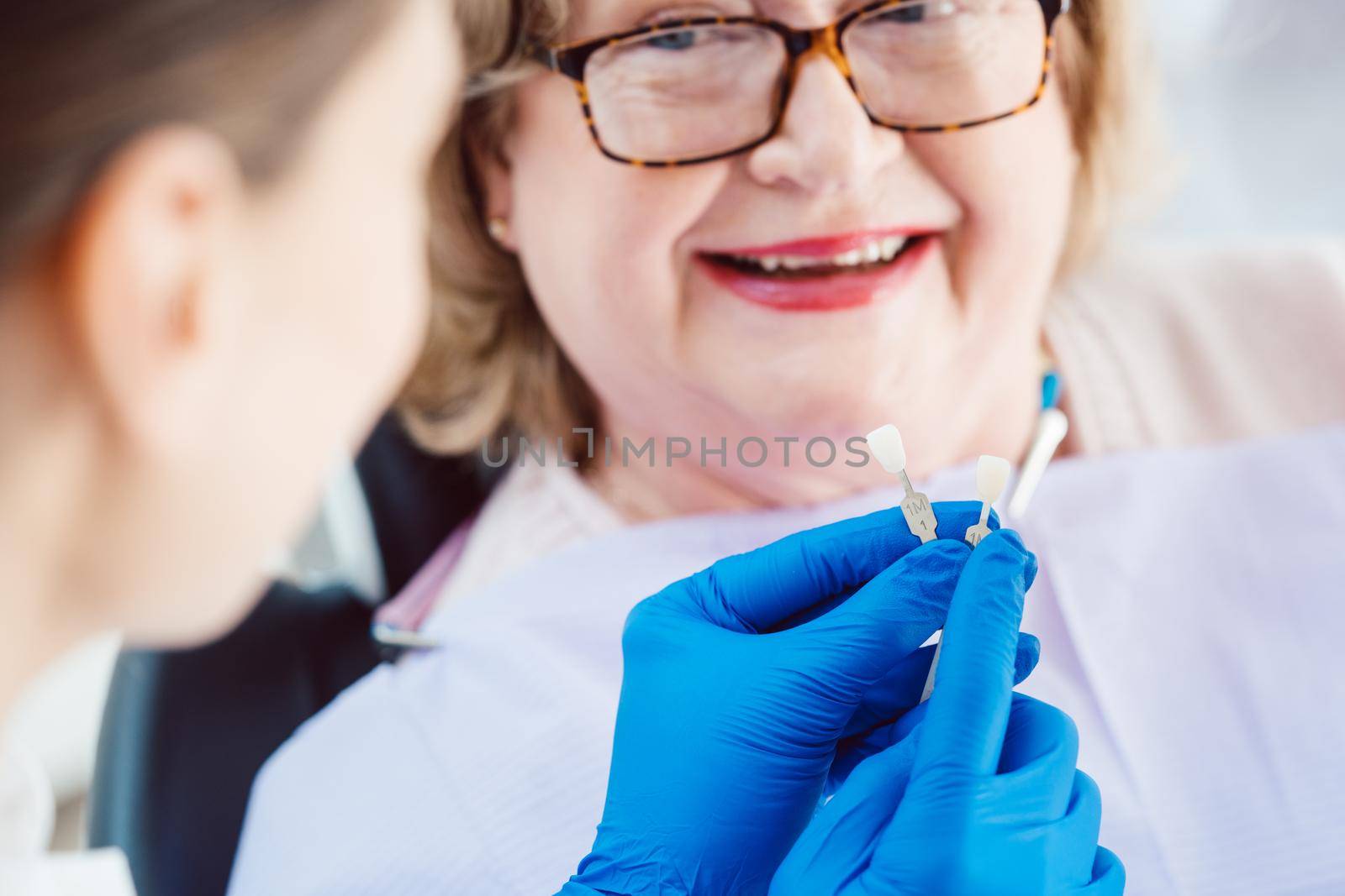 Dentist showing senior patient samples of teeth colors before dental bleaching counseling her