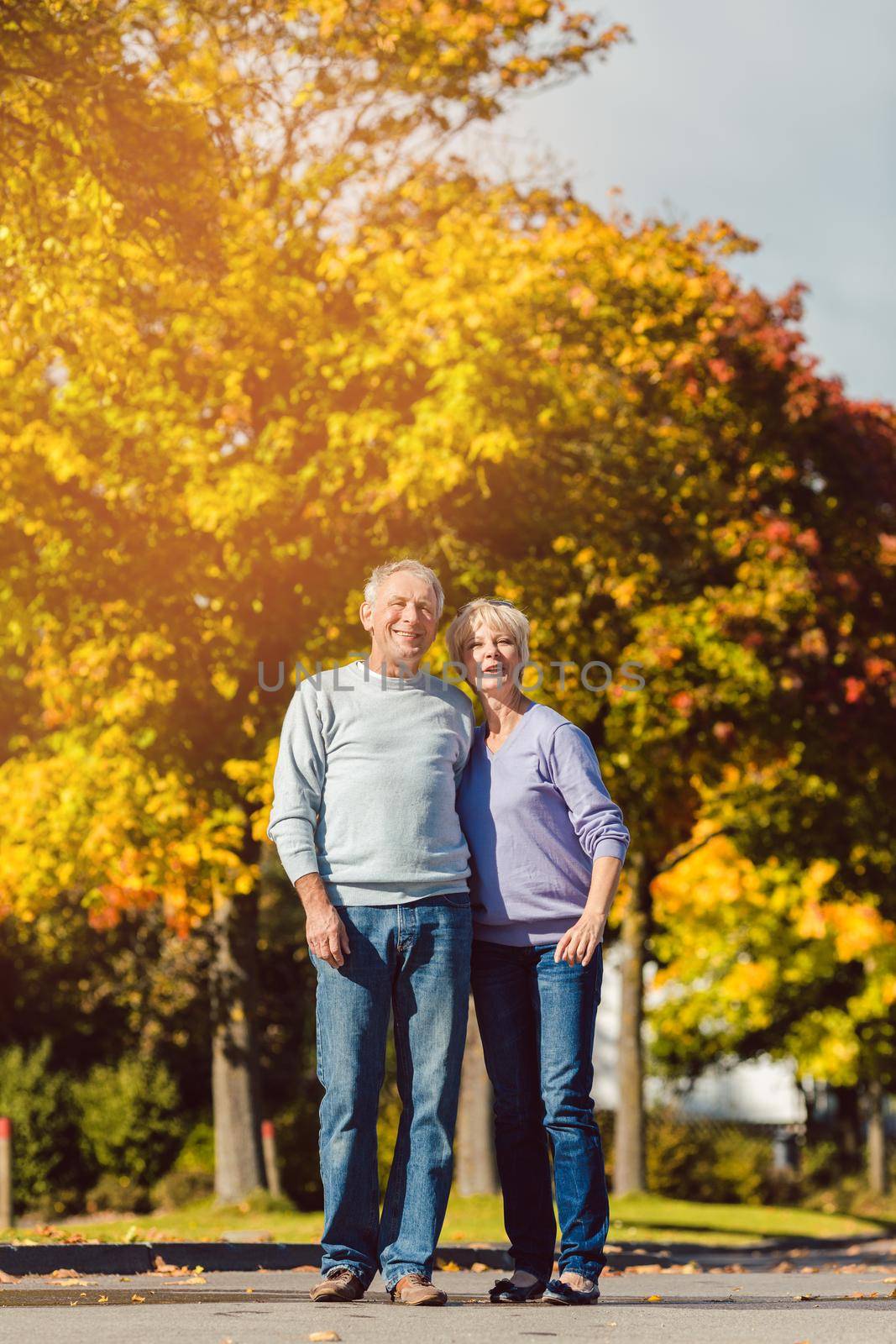 Man and woman, senior couple, having a walk in autumn or fall outdoors, the trees show colorful foliage