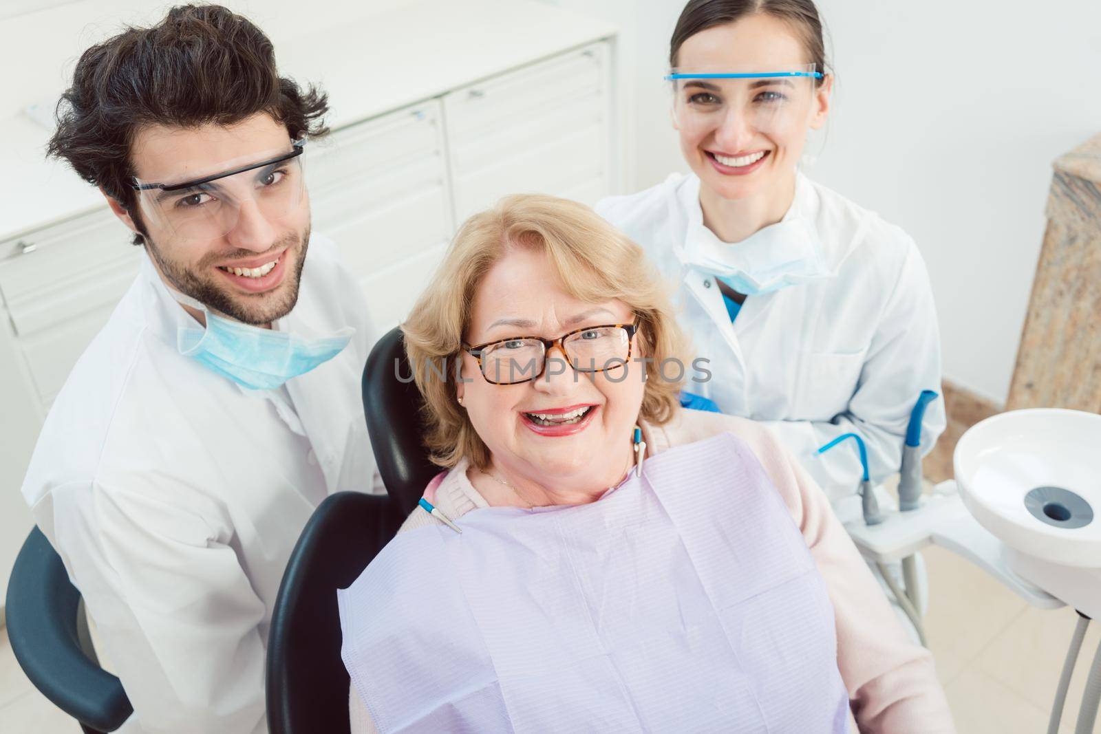 Dentists and patient in surgery looking at camera by Kzenon
