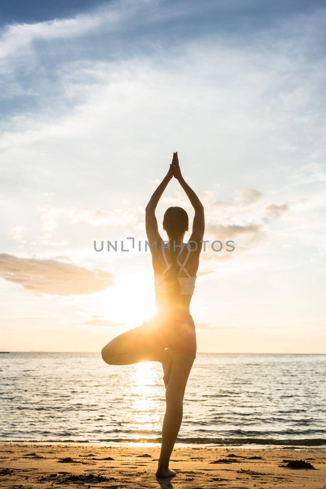 Silhouette of a woman practicing the tree yoga pose on a beach by Kzenon