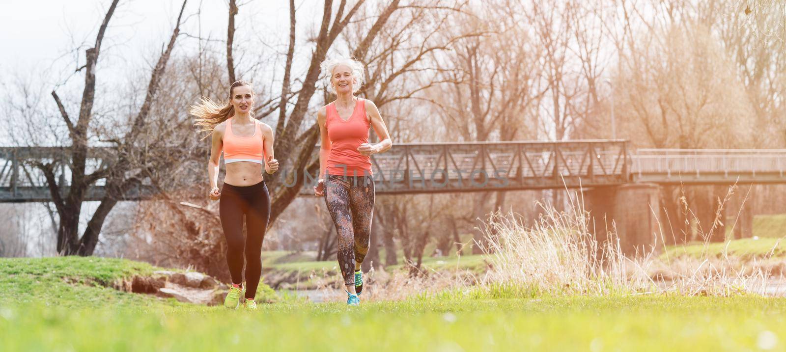 Senior and young woman running as sport on a meadow in spring towards the viewer