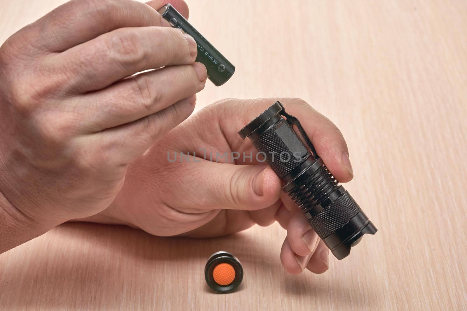 Hands hold a small black flashlight and replace the battery in it. Close up