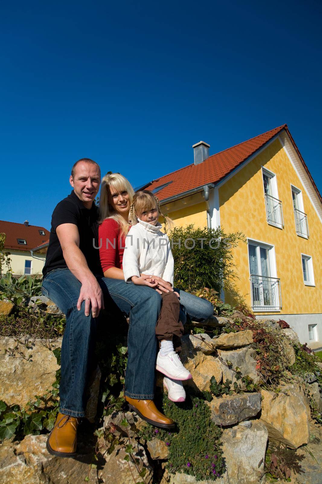 A young couple with their daughter sitting in front of their yellow home
