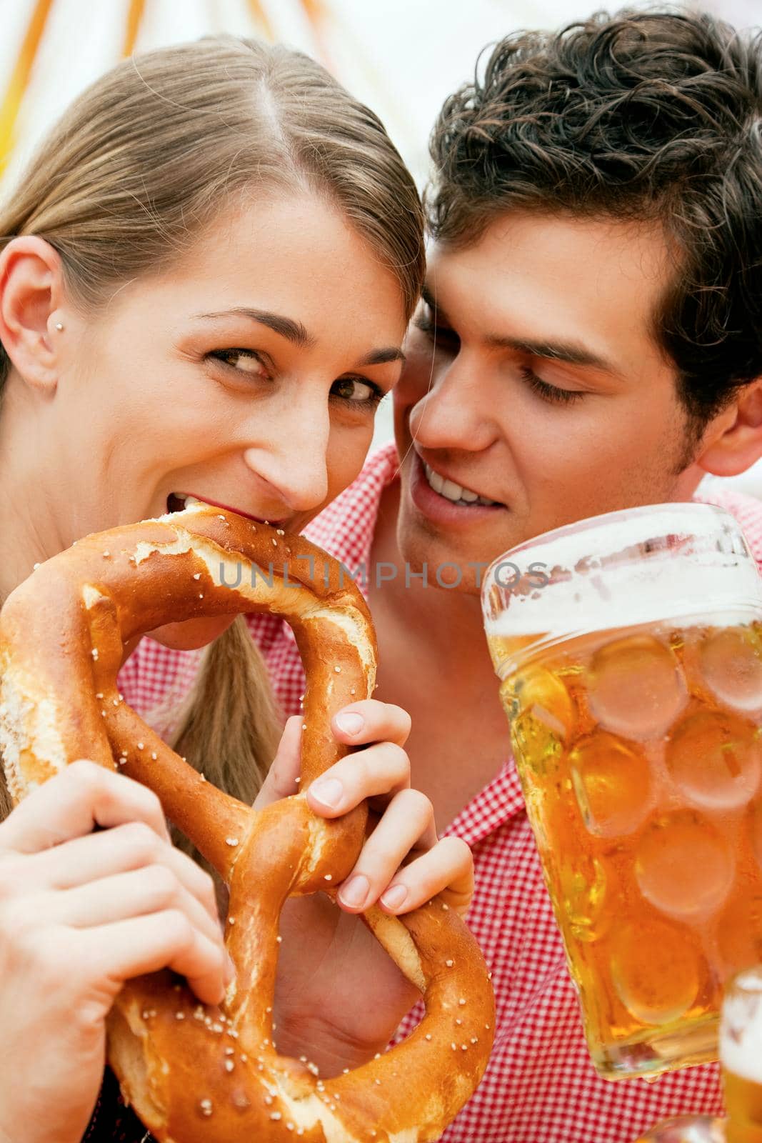 Couple in traditional German costume in a beer tent, he is having a drink, she a pretzel, scene could be located at the Oktoberfest or any Dult