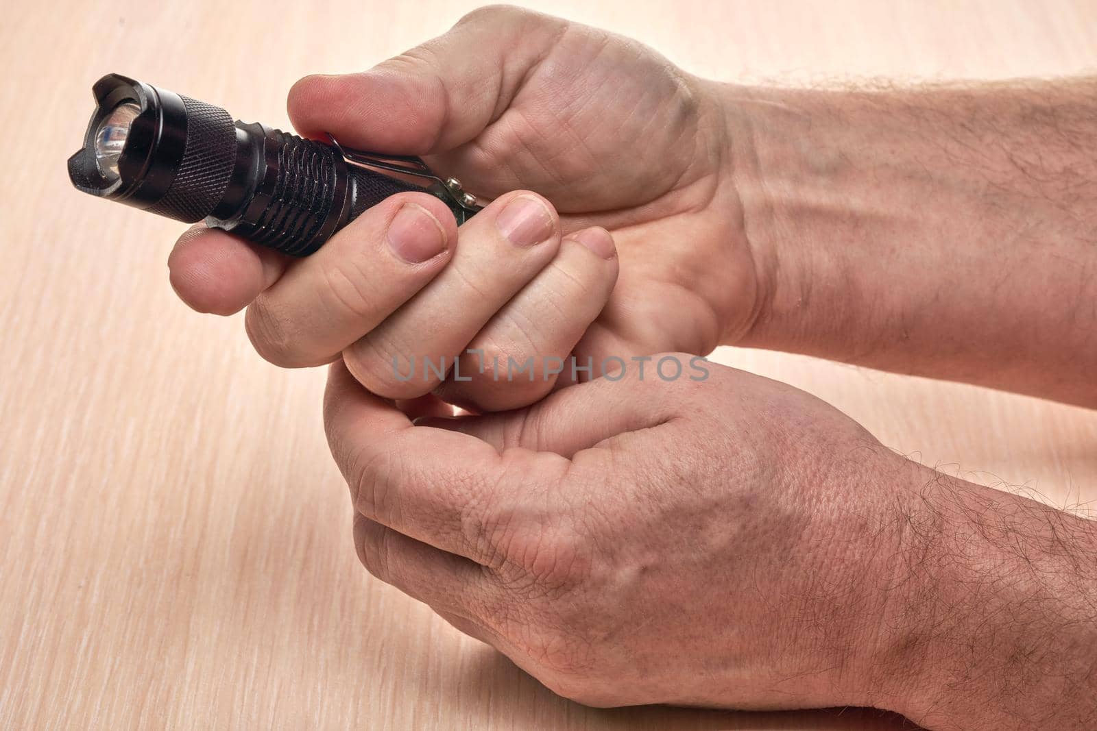 Hands hold a small black flashlight to replace the used battery. Close up