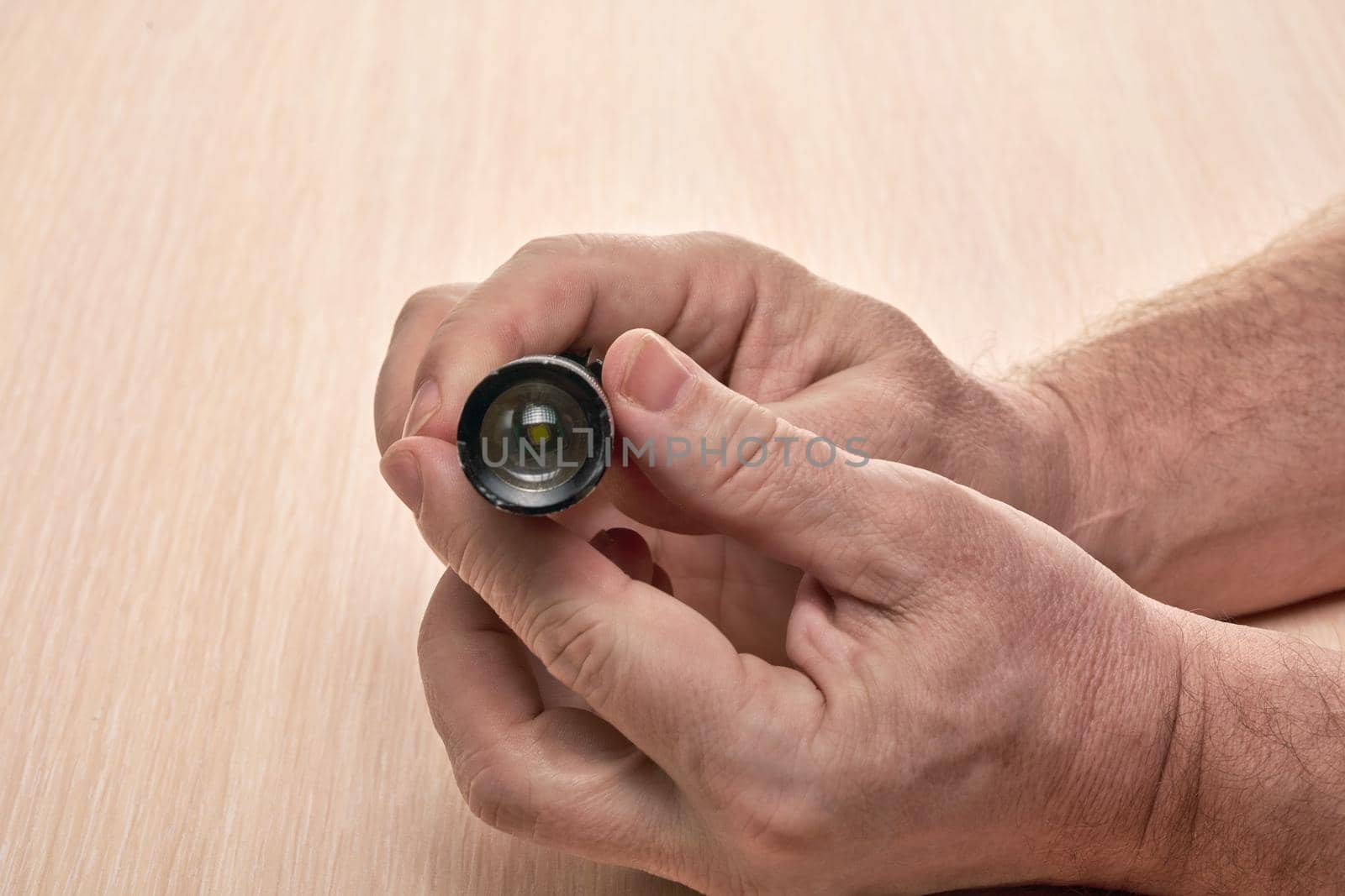 Hands hold a small black flashlight aimed at the camera. Close up