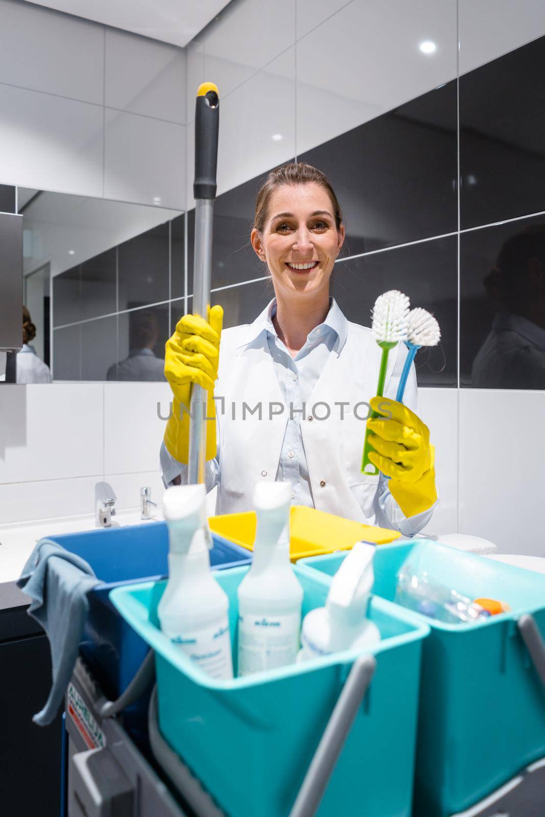 Janitor or charlady with her work tools looking at camera in toilet by Kzenon