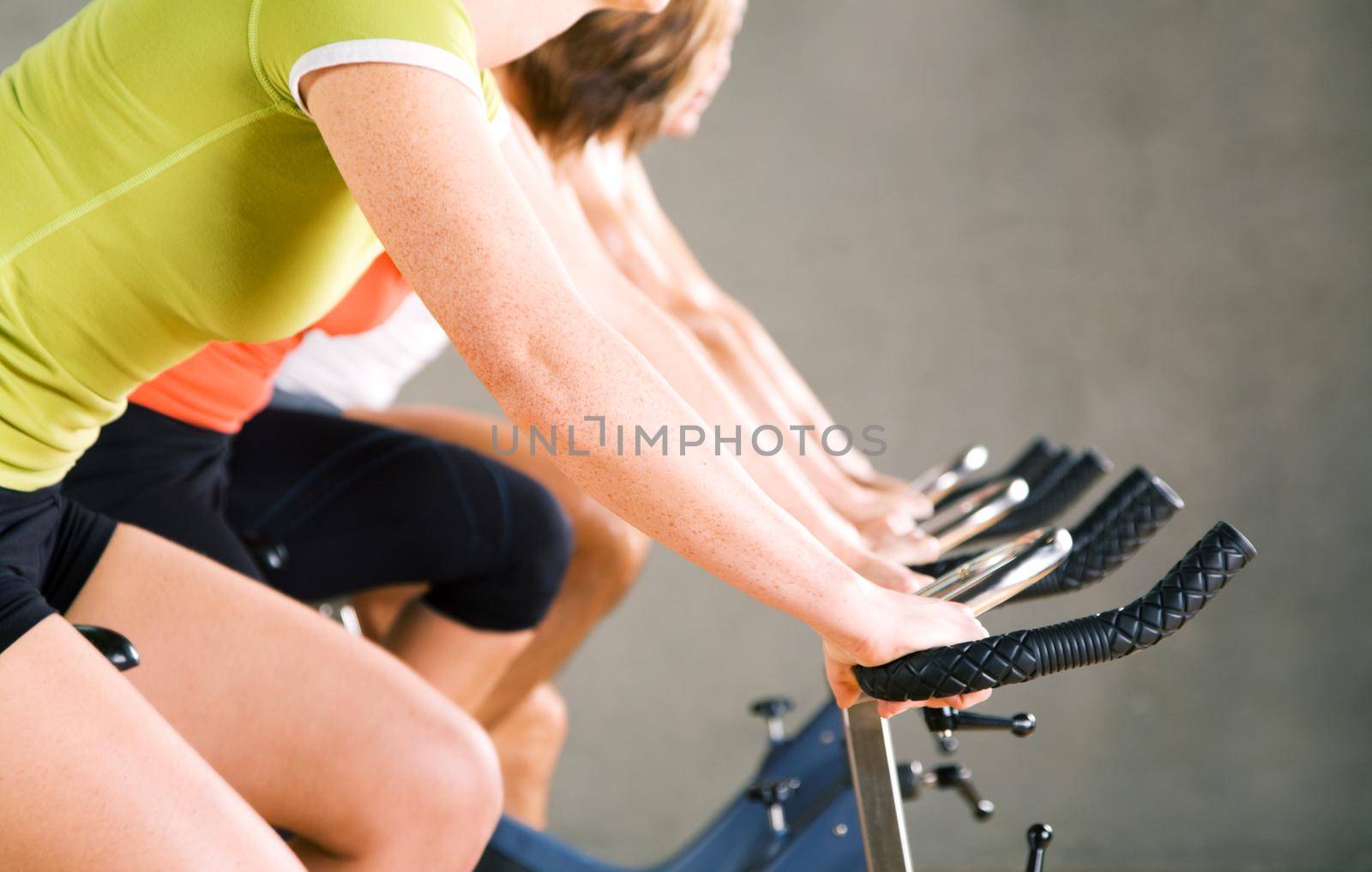 Three people working out on a stationary bicycle in the gym